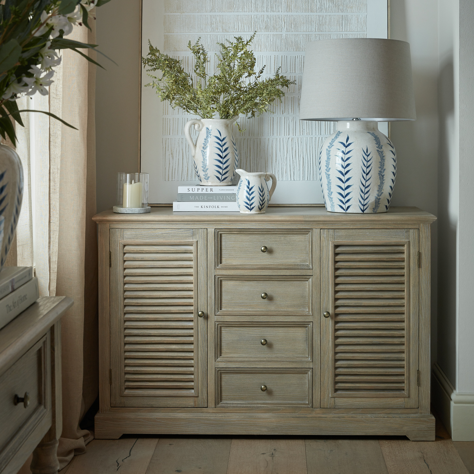 The Deauville two door, four drawer large dresser base is shown dressed with lamp, vase and books