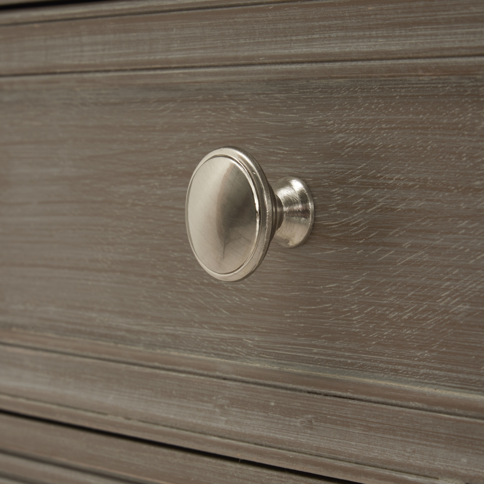 The image shows a brass coloured, round handle on the front of a wooden drawer