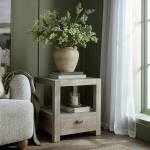The image shows a chunky, square, side table next to a sofa, there is a drawer at the bottom of the side table and an open frame between the drawer and the top of the cabinet, with wooden uprights at each corner.